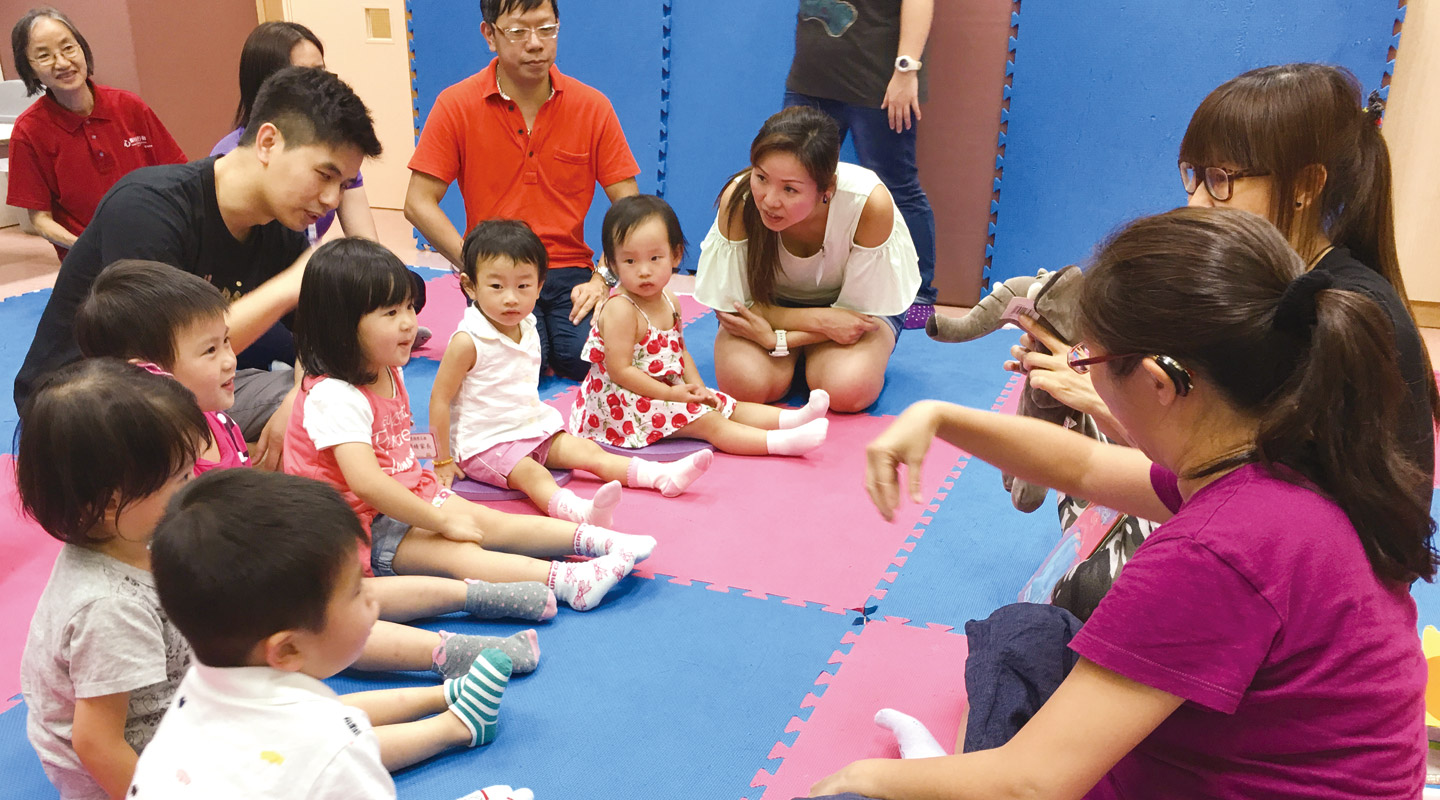 Toddlers and their parents engaging in a sign class led by a deaf and a hearing teacher