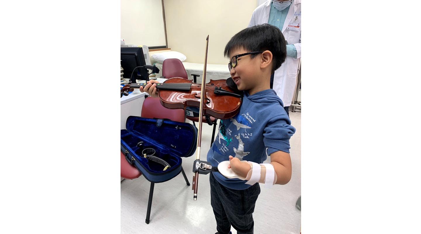 A child learning to play the violin with his ‘new hand’ 